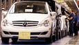 Un automóvil Mercedes-Benz blanco en una línea de ensamblaje de fábrica con trabajadores.