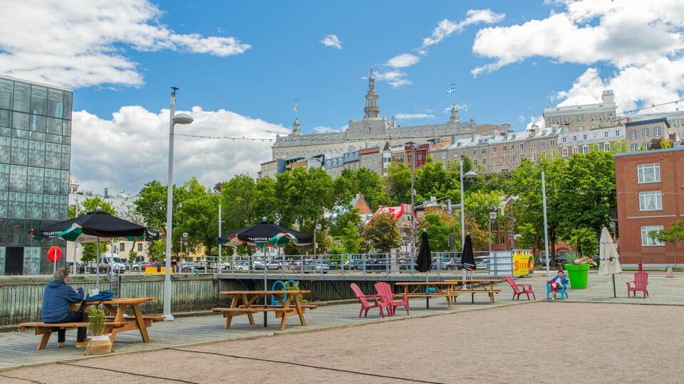 En park med picnicborde og stole, en moderne bygning og en historisk bygning med et tårn.