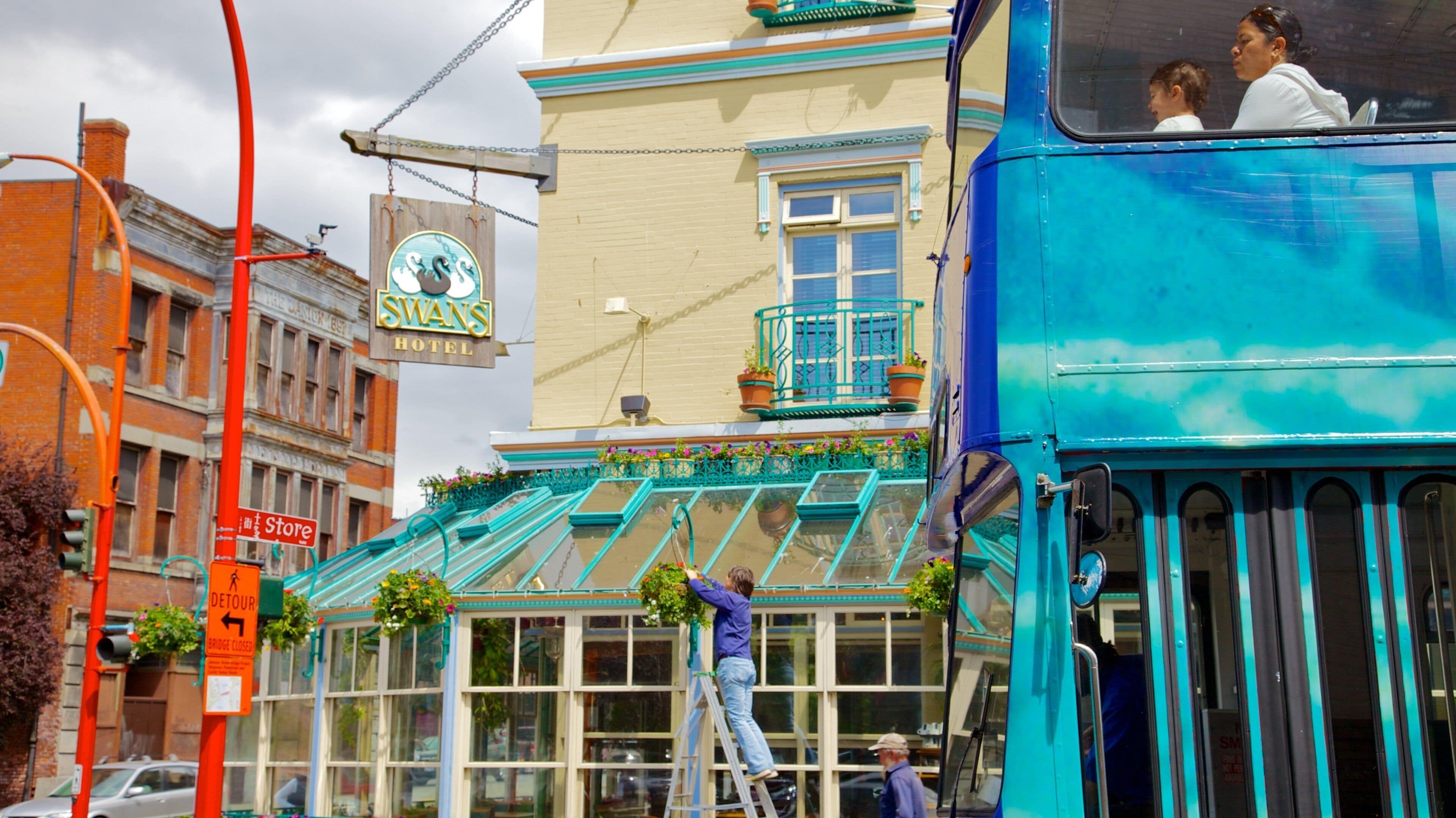 Un autobus à deux étages bleu est garé devant un immeuble sur lequel on peut lire l’inscription « Hôtel Swans ».