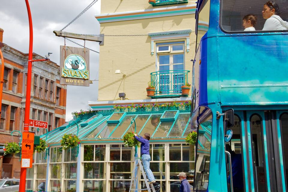 Un autobus à deux étages bleu est garé devant un immeuble sur lequel on peut lire l’inscription « Hôtel Swans ».