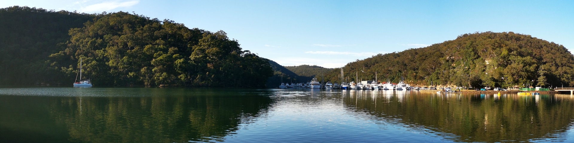 A calm lake with boats docked on the right, surrounded by forested hills.