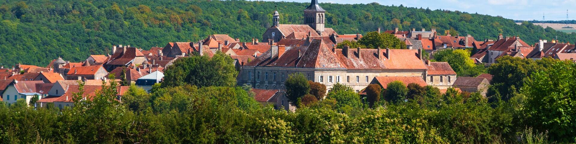 A town with red-roofed buildings, a prominent church with a tall steeple, and a lush green hillside in the background.