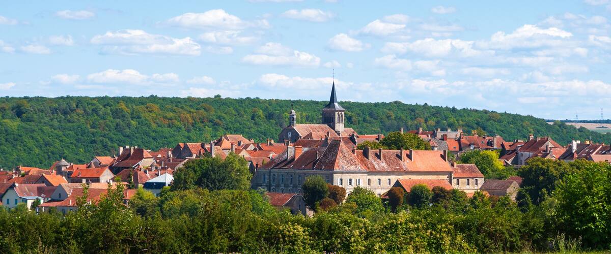 A town with red-roofed buildings, a prominent church with a tall steeple, and a lush green hillside in the background.