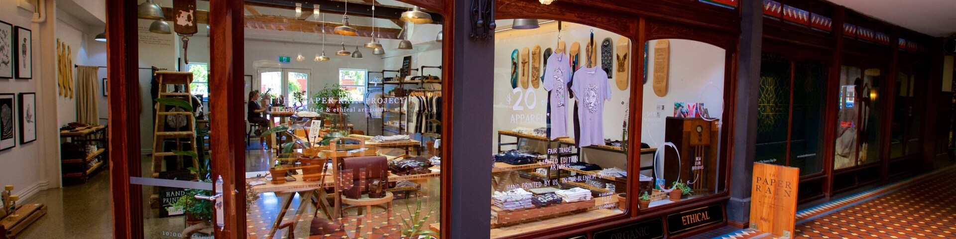 Fachada com placas que dizem 'HANDCRAFTED' e 'FAIR TRADE', vitrines de madeira e piso estampado.