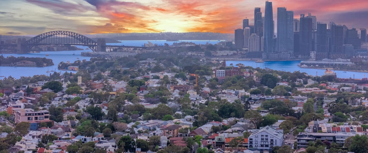 A cityscape with a prominent bridge, a cluster of high-rise buildings, and a sunset sky.