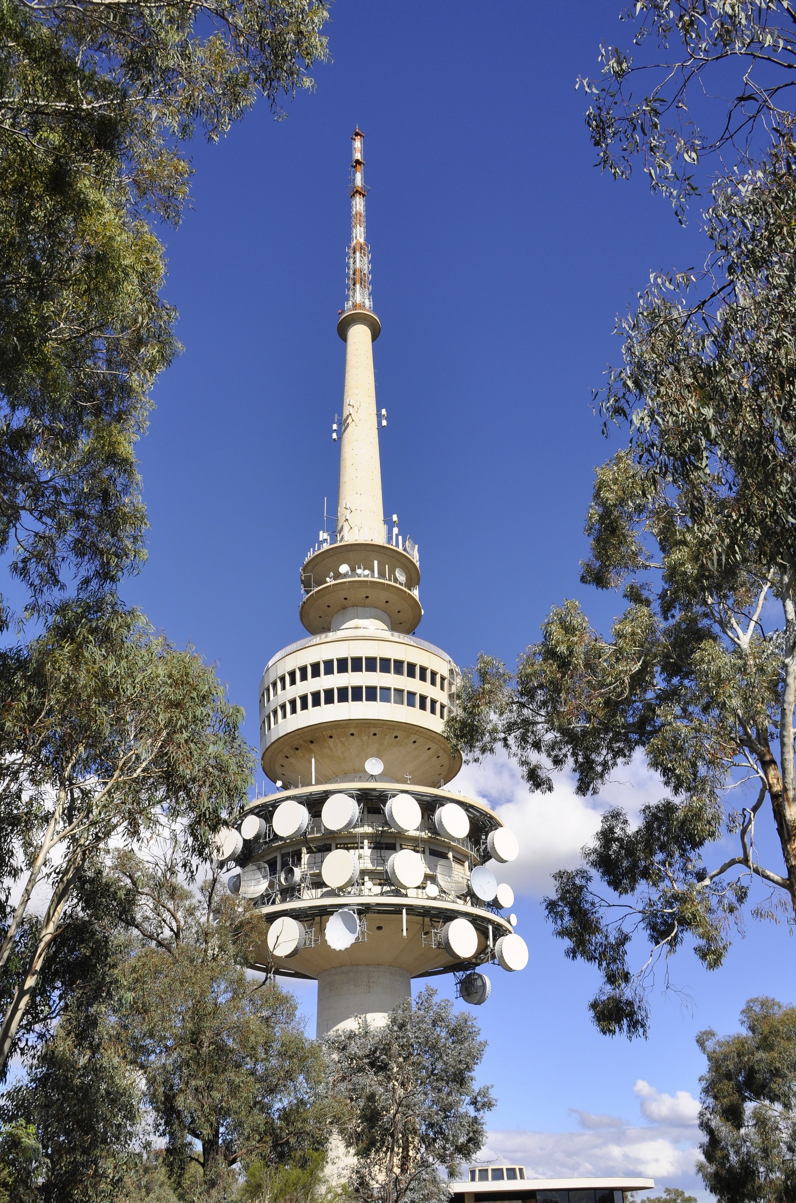 A tall tower with multiple circular platforms and antennas, surrounded by trees.
