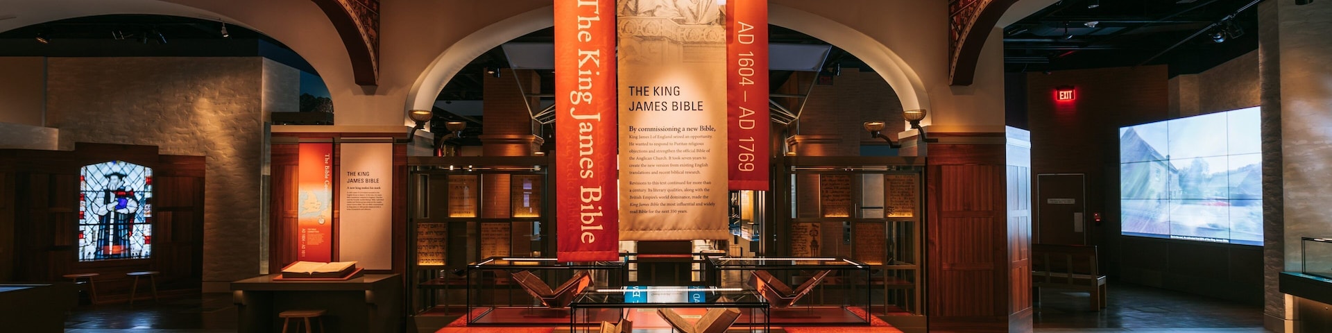 Interior de museu com uma vitrine exibindo a Bíblia King James, cercada por painéis informativos e faixas.