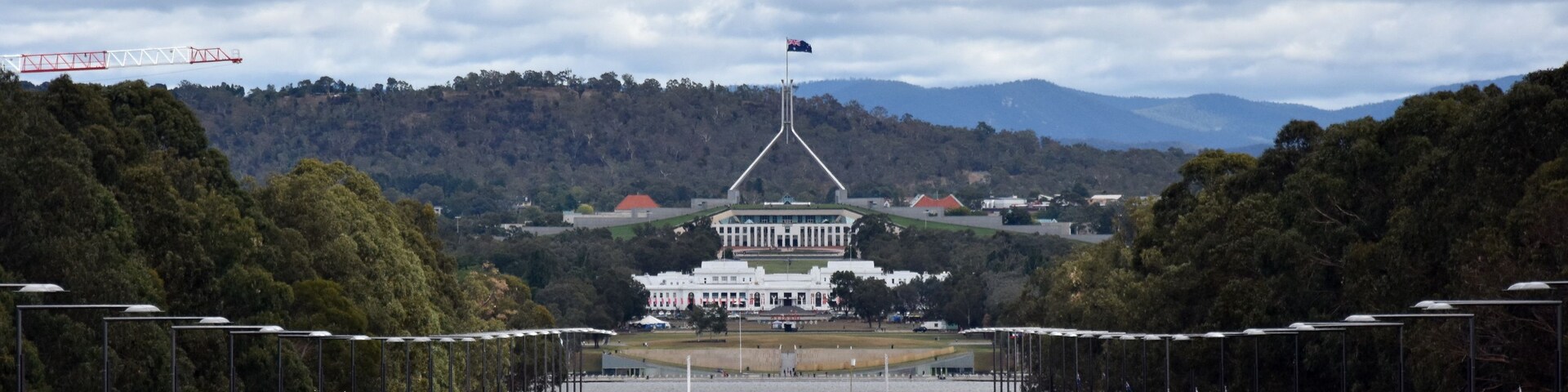 A wide road leading to a large white building with a flag on top, surrounded by trees and hills.