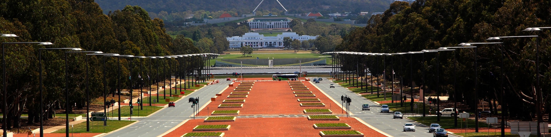 A wide road with a red surface leading to a large white building with a flagpole.