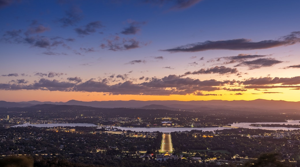 A cityscape at dusk with a river, mountains in the background, and a bridge.