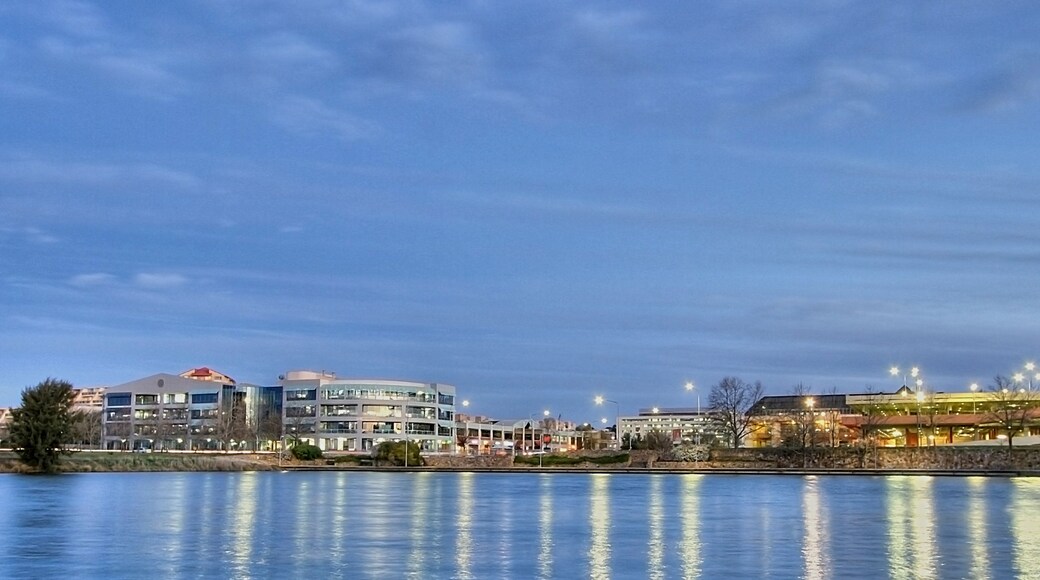 A calm lake reflecting buildings and a clear sky.