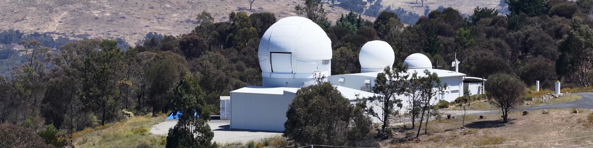 A white observatory with two domes, surrounded by trees and hills.