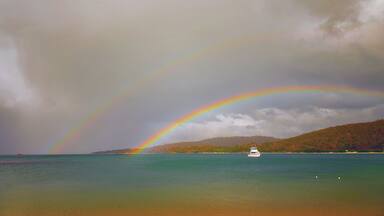 A boat on a calm sea with a rainbow arching over it.