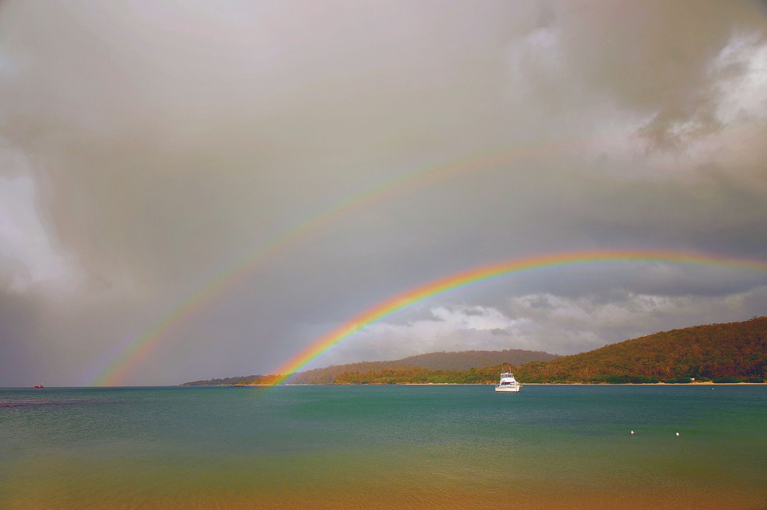 A boat on a calm sea with a rainbow arching over it.