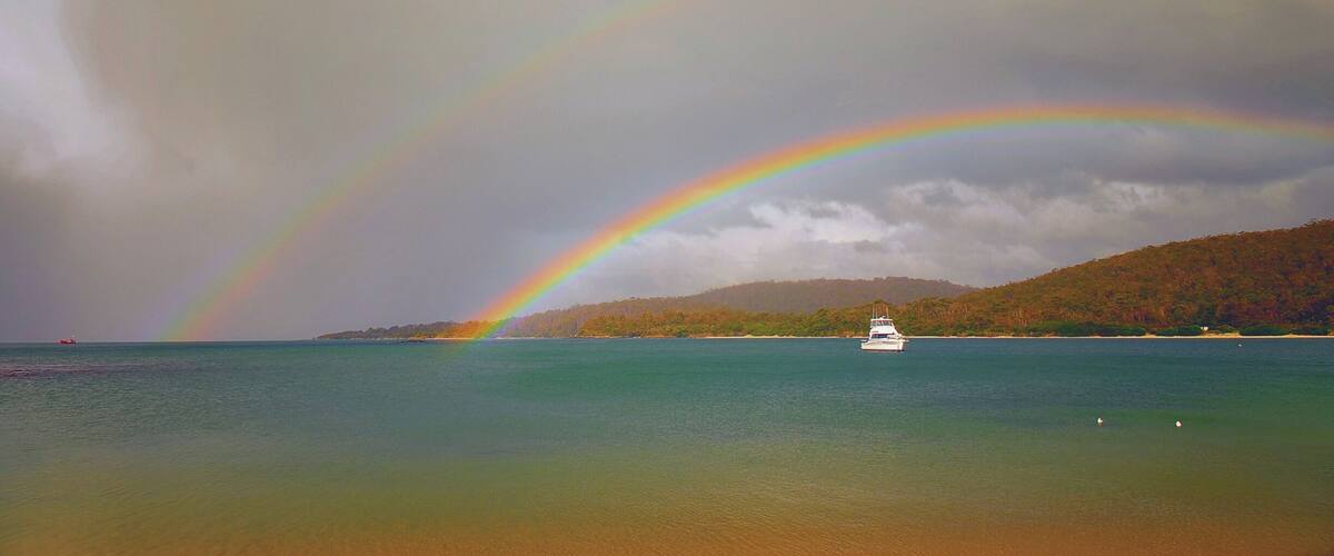 A boat on a calm sea with a rainbow arching over it.