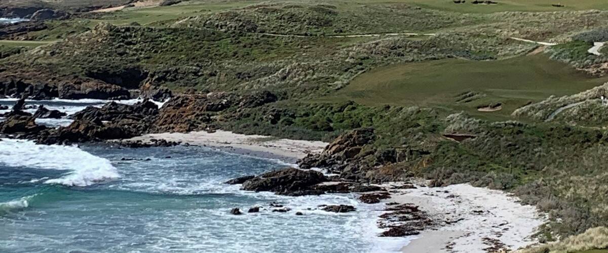 A coastal landscape with a lighthouse on a grassy hill, rocky shoreline, and waves crashing onto the beach.