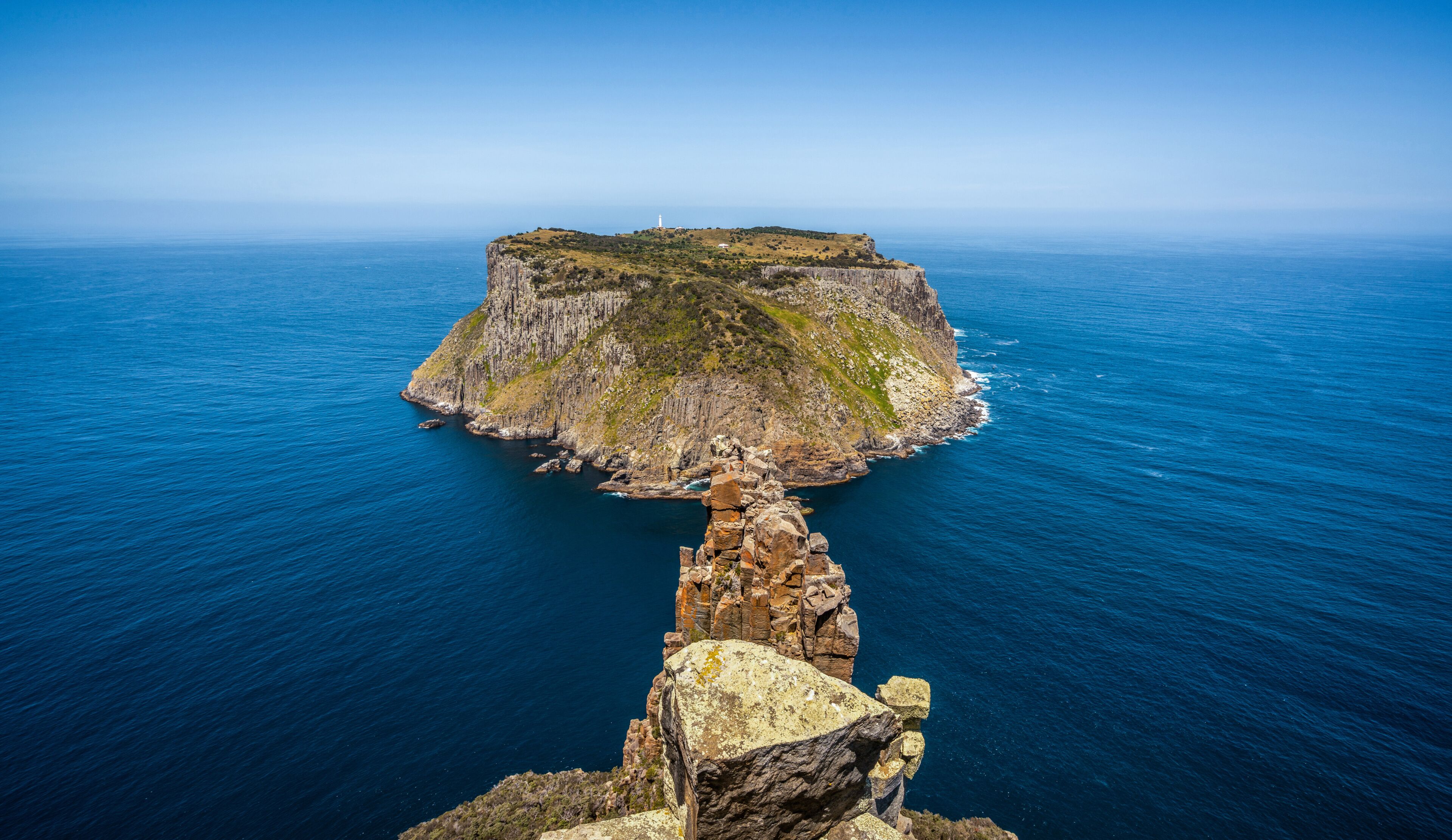 A coastal cliff with a lighthouse and a rocky outcrop in the foreground.