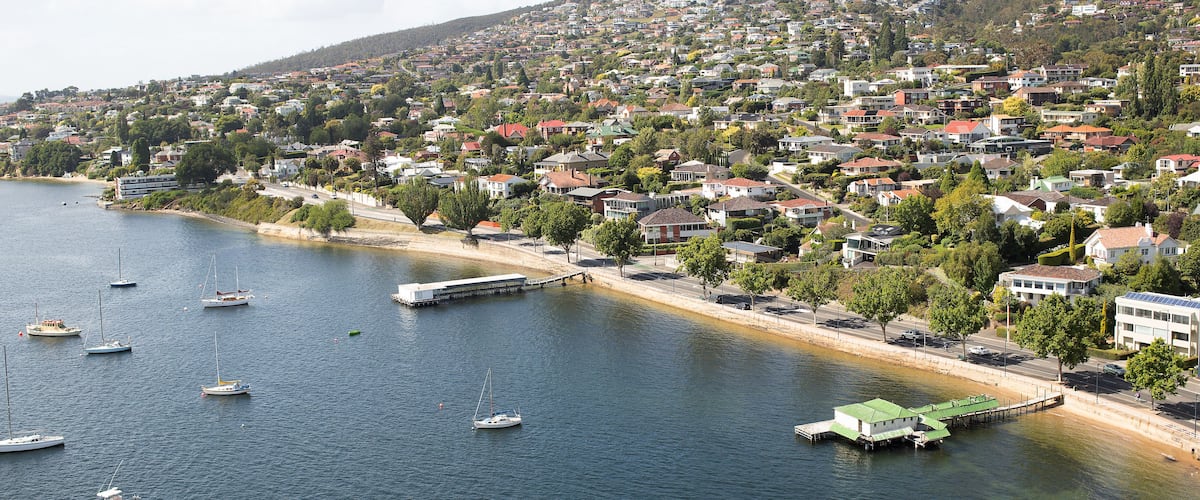 A coastal town with houses, a marina with boats, and a hilly backdrop.