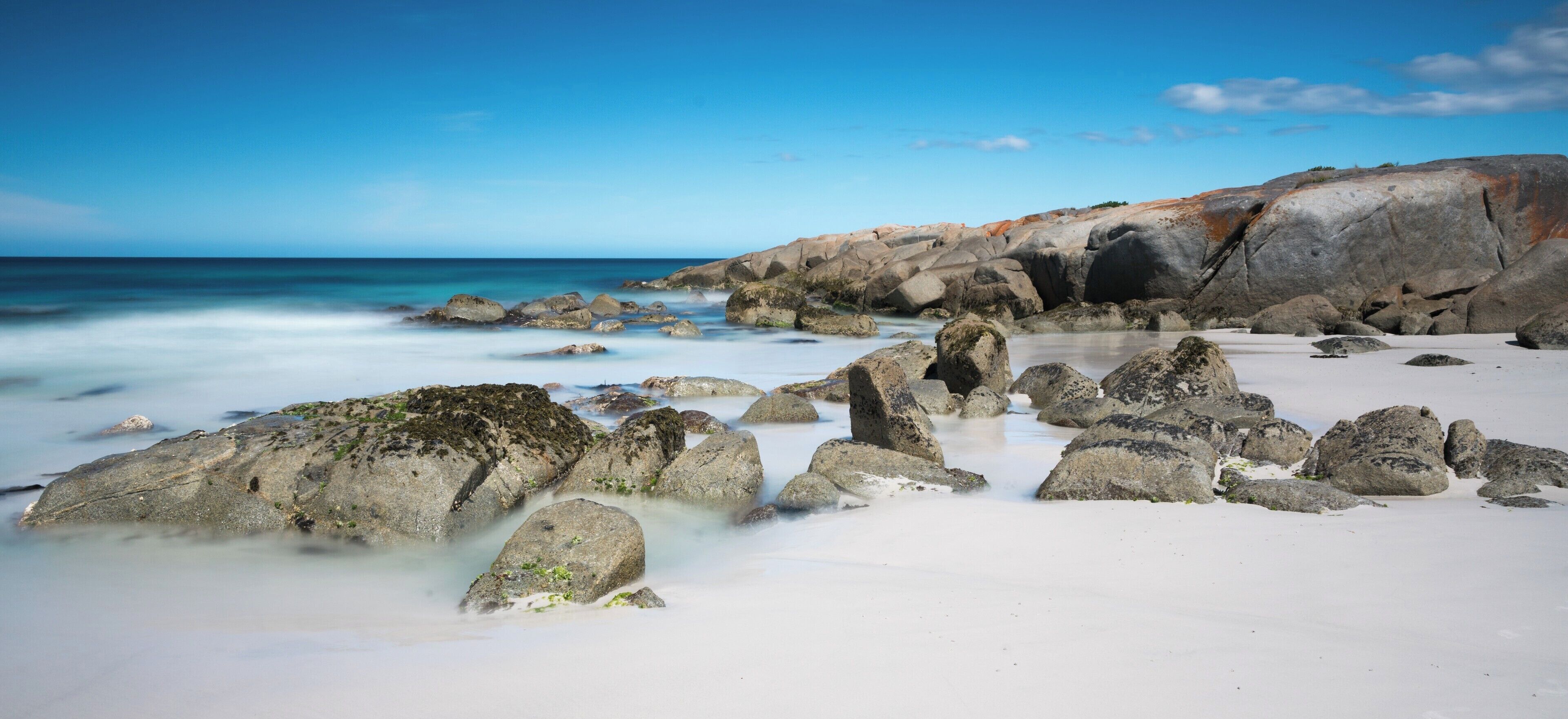 A rocky beach with white sand and clear blue water.