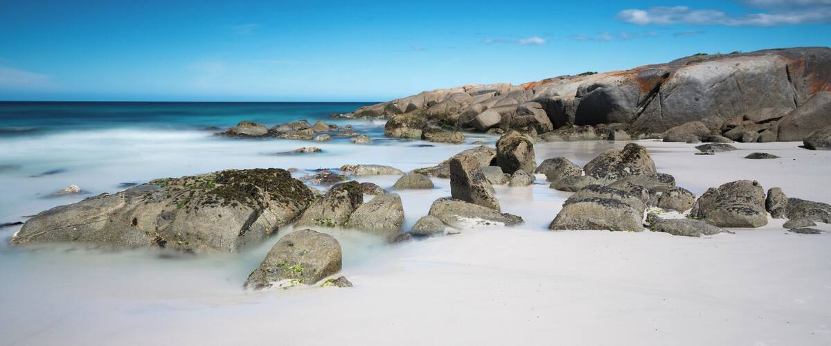 A rocky beach with white sand and clear blue water.