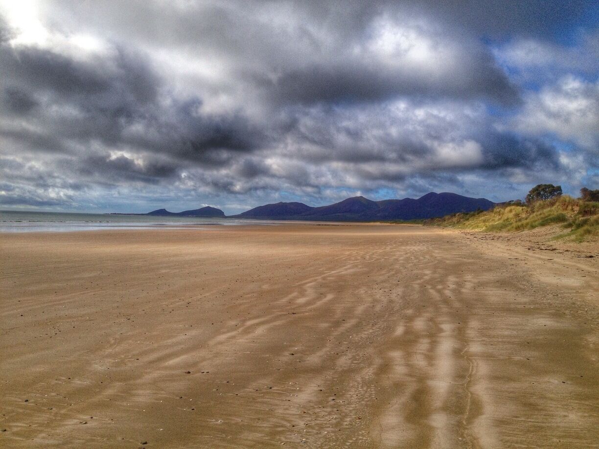 A sandy beach with distant mountains under a cloudy sky.