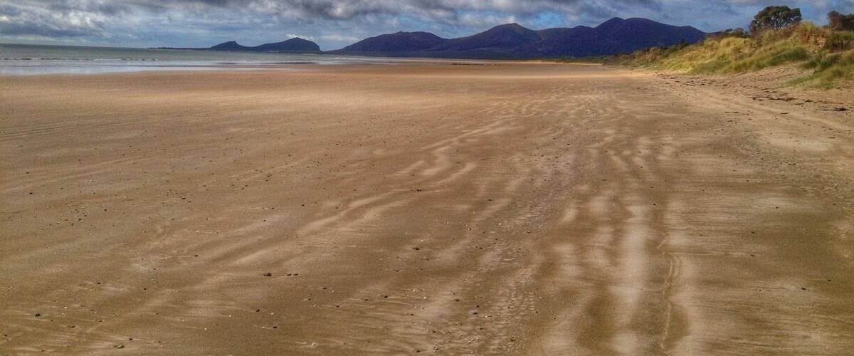 A sandy beach with distant mountains under a cloudy sky.