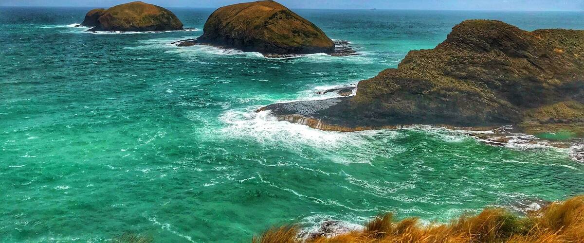 A coastal landscape with three prominent rocky outcrops surrounded by turquoise waters.