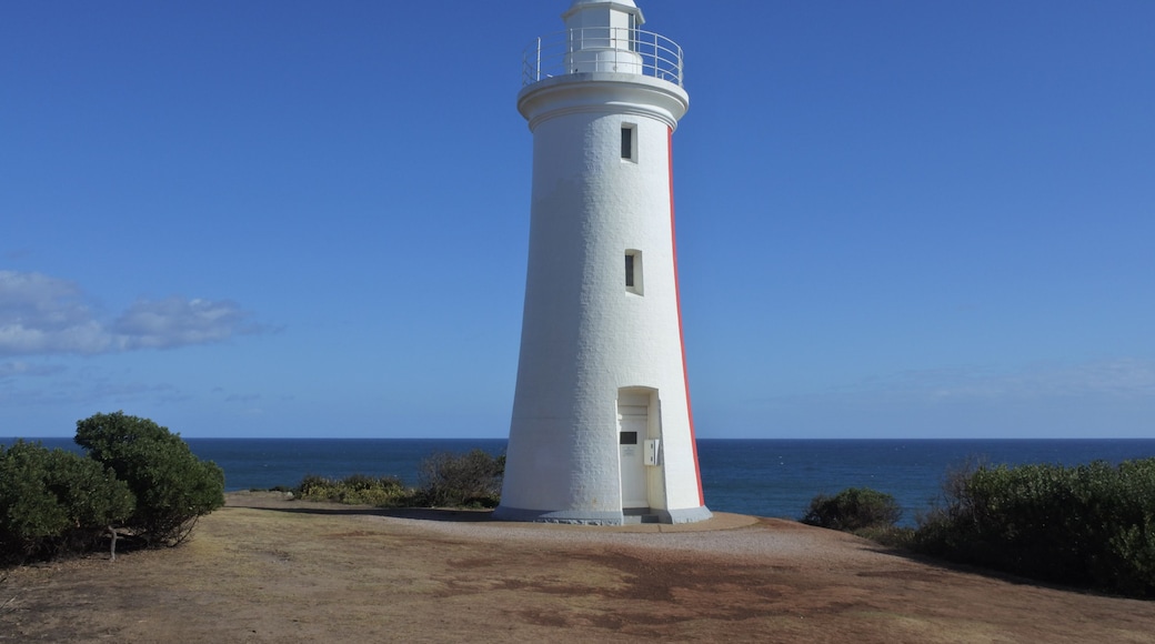 A white lighthouse with a red stripe, surrounded by a clear blue sky and the ocean.
