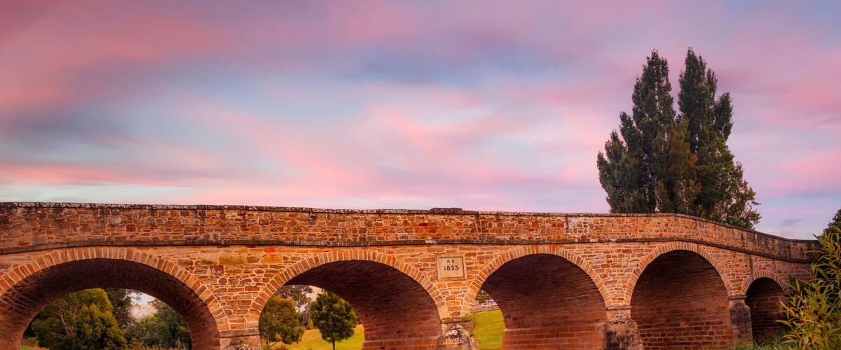 Un puente de piedra con múltiples arcos sobre un río tranquilo, rodeado de vegetación y árboles.