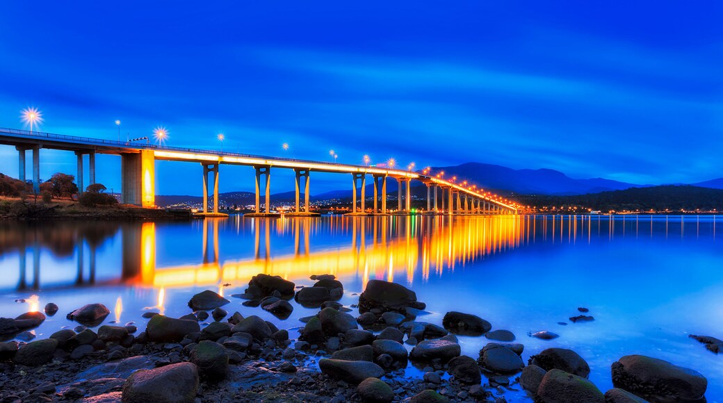 A long bridge with lights reflecting on a calm body of water at night.