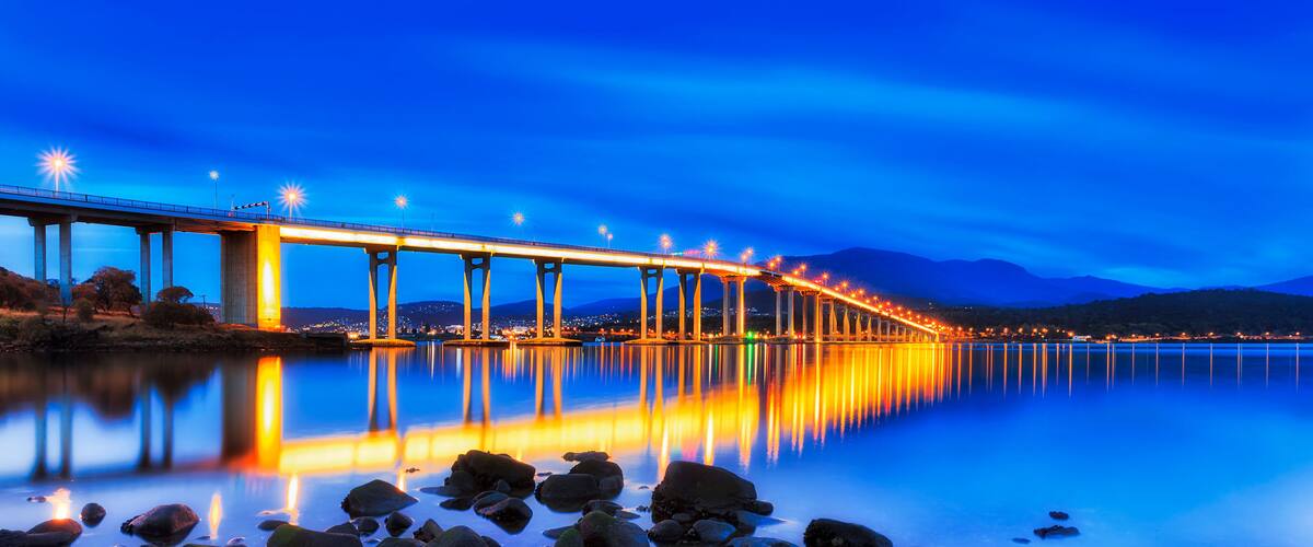 A long bridge with lights reflecting on a calm body of water at night.