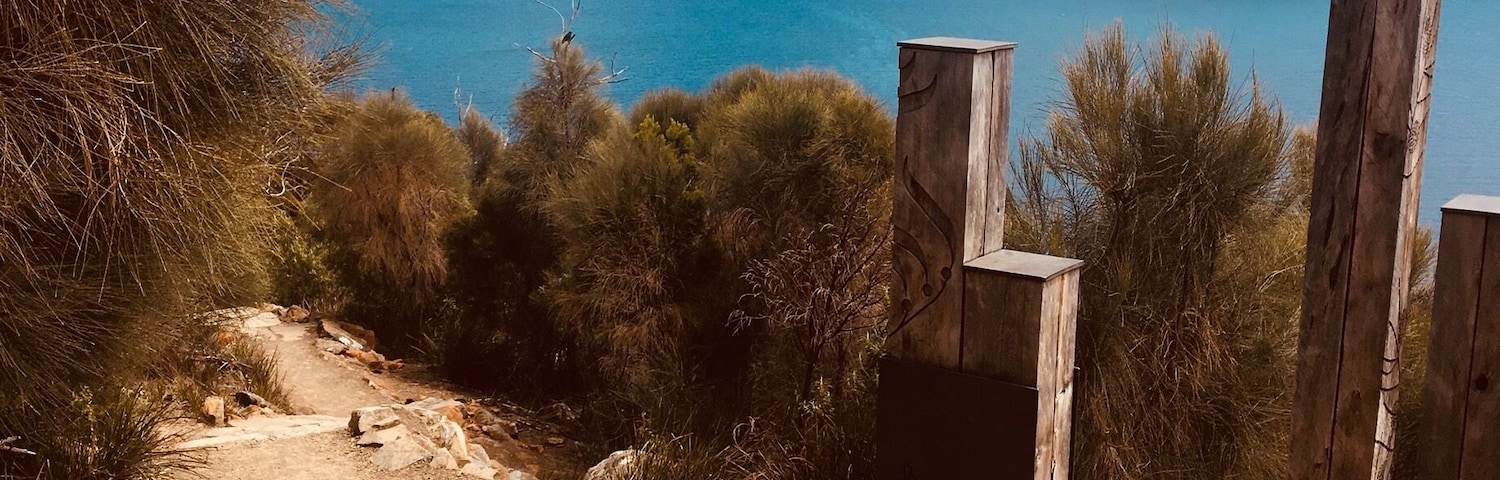 Un paisaje costero con mar azul cristalino, terreno rocoso y una estructura de madera.