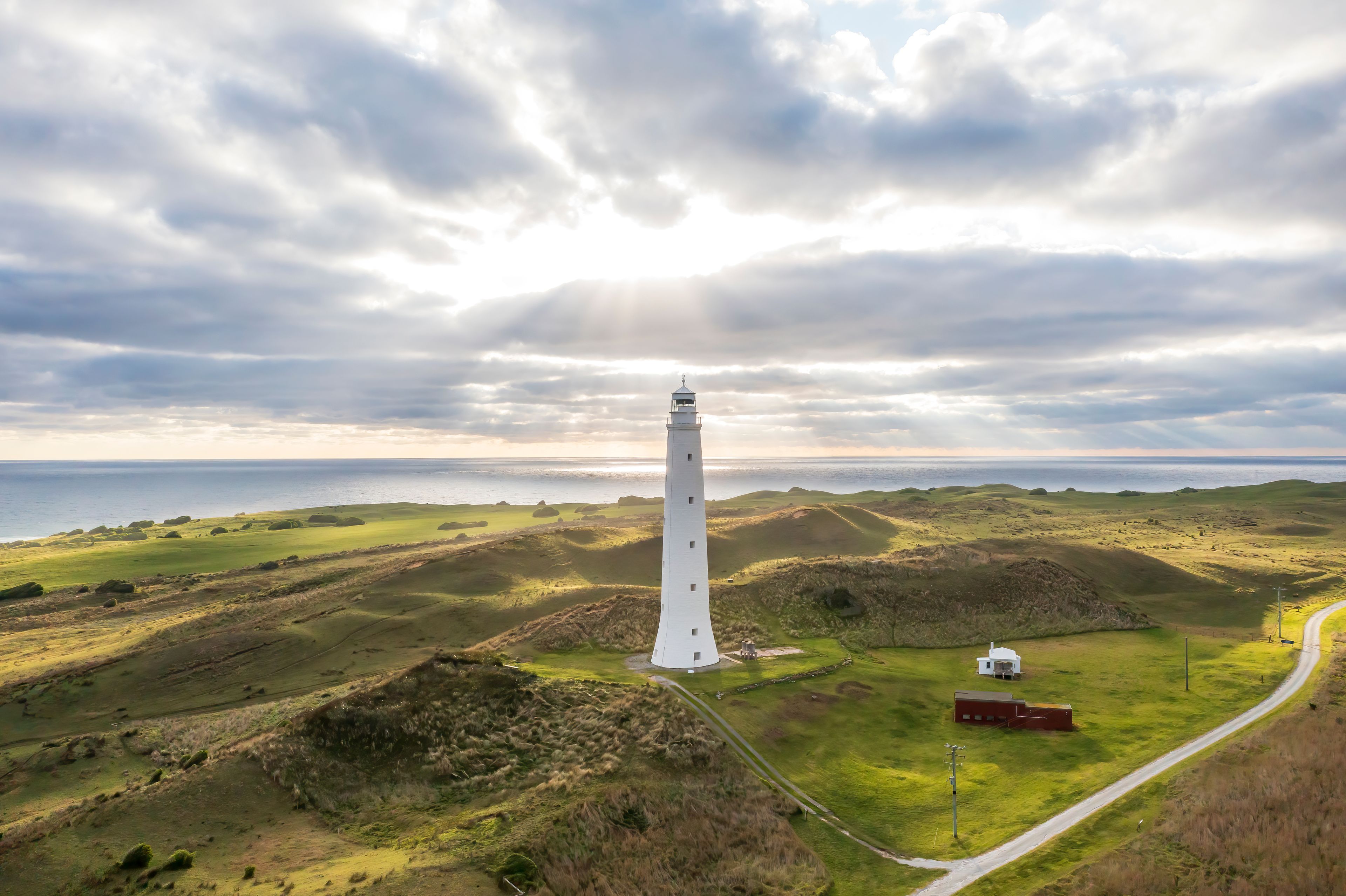 Un faro blanco en una colina cubierta de hierba con vista al océano y cielo nublado.