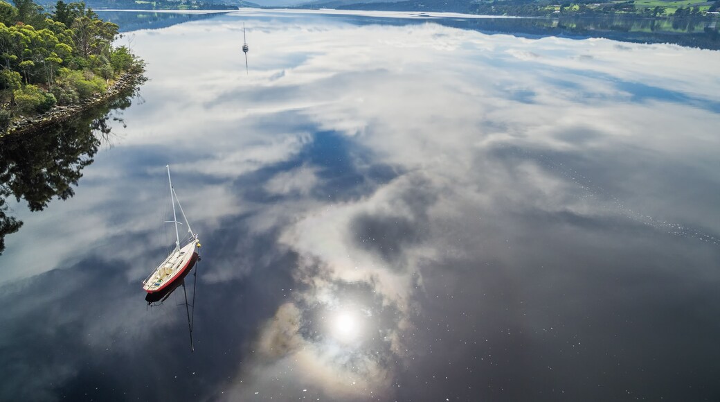 A calm lake with a sailboat, surrounded by mountains and a clear sky.