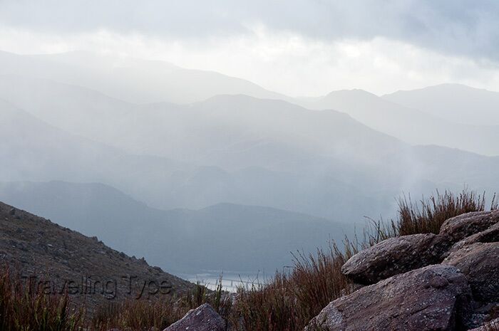 A mountainous landscape with rocky terrain and distant fog-covered peaks.