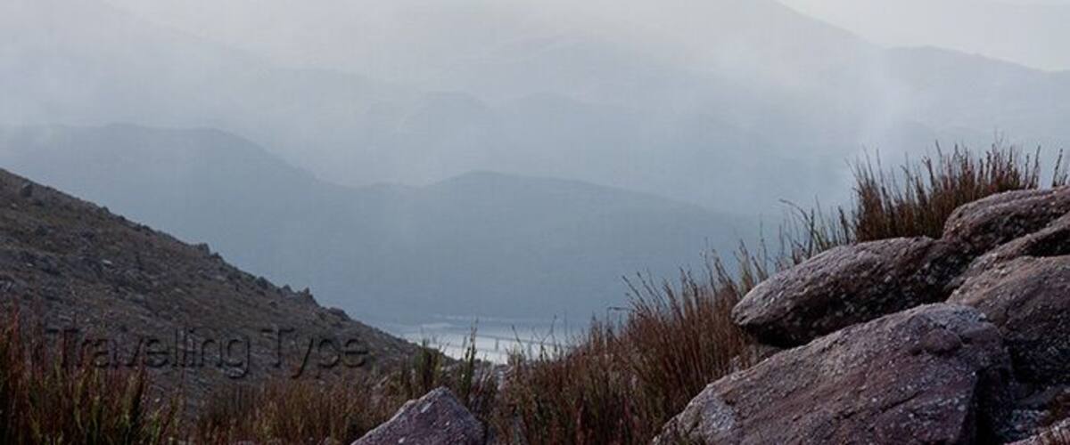 A mountainous landscape with rocky terrain and distant fog-covered peaks.