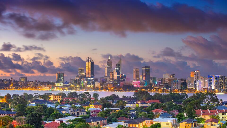 A city skyline at dusk with illuminated buildings and a river in the foreground.