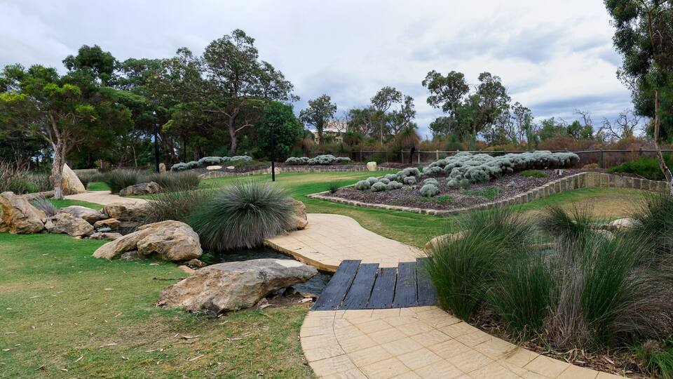 A landscaped garden with a wooden bridge, large rocks, and various shrubs.