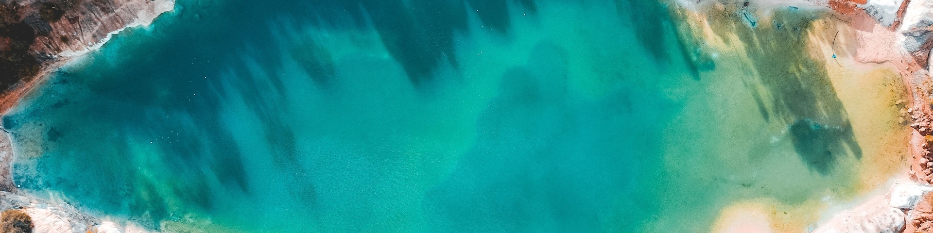 Vista aérea de un lago grande de color turquesa rodeado por terreno marrón rojizo y vegetación escasa.