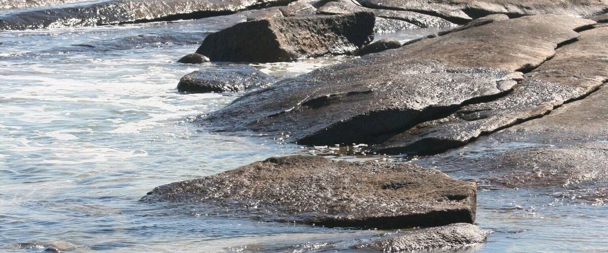 A rocky shoreline with clear water and waves crashing against the rocks.