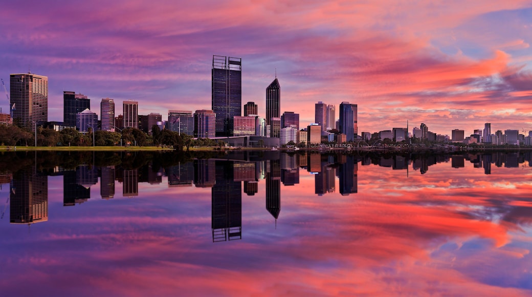 A city skyline at sunset with reflections in a calm body of water.