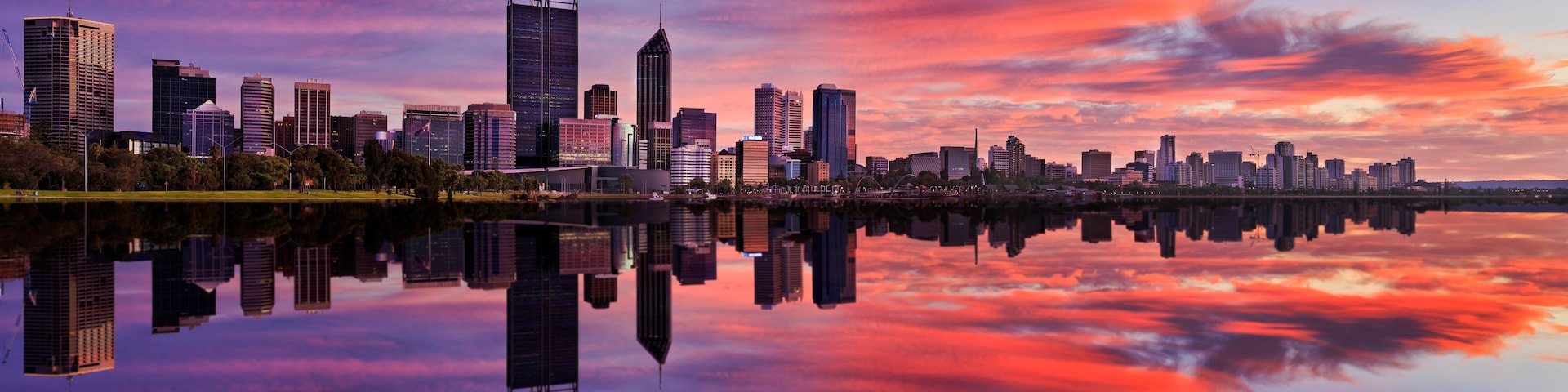 A city skyline at sunset with reflections in a calm body of water.