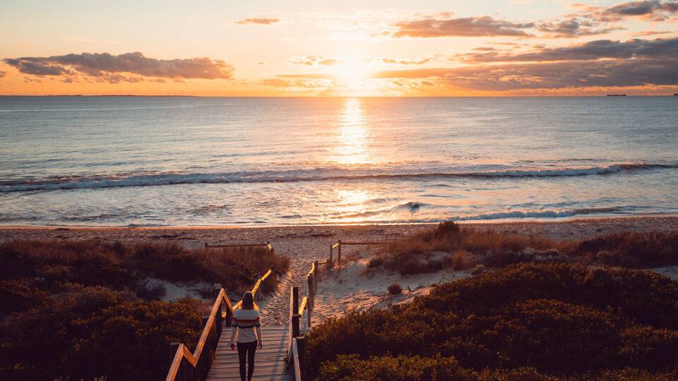 A wooden boardwalk leading to a beach at sunset.