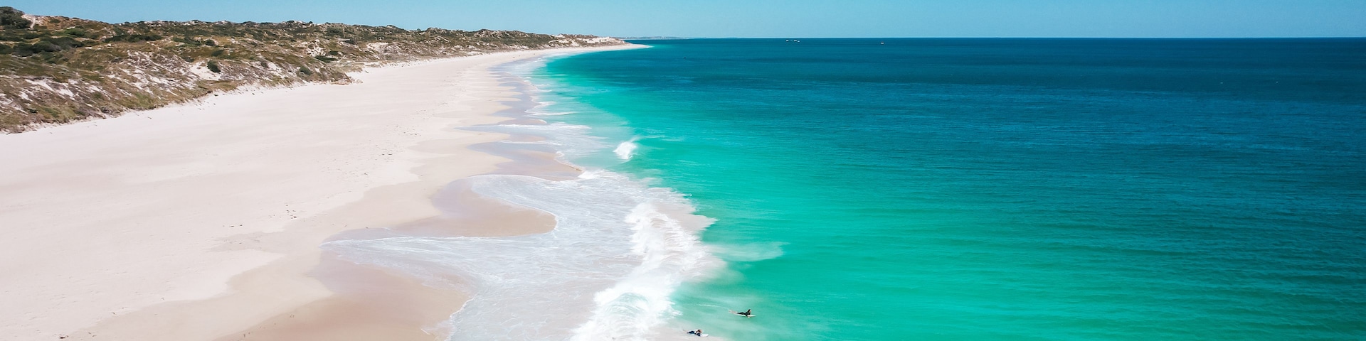 A beach with clear turquoise waters and a sandy shoreline.