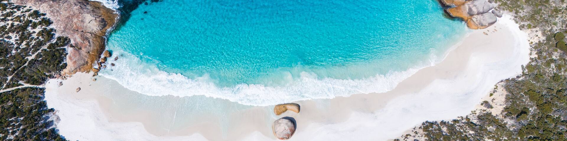 A coastal landscape with clear turquoise waters, sandy beaches, and rocky outcrops.
