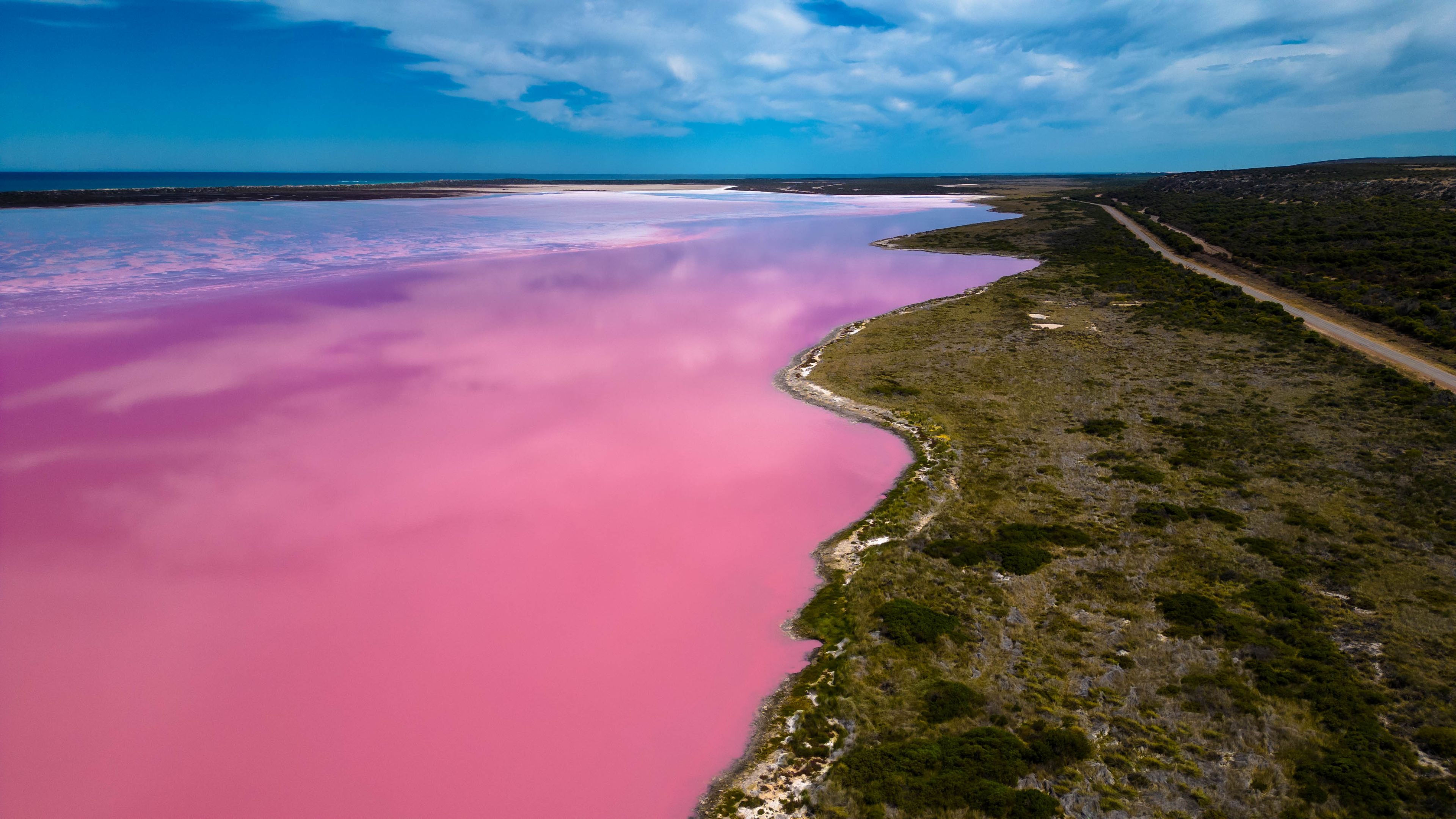 Un lac rose, entouré d’une végétation verdoyante, sous un ciel bleu azur.