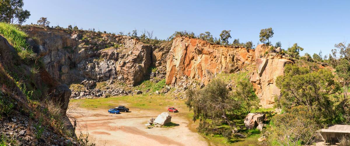 A rocky cliff with a steep drop, surrounded by greenery and trees.