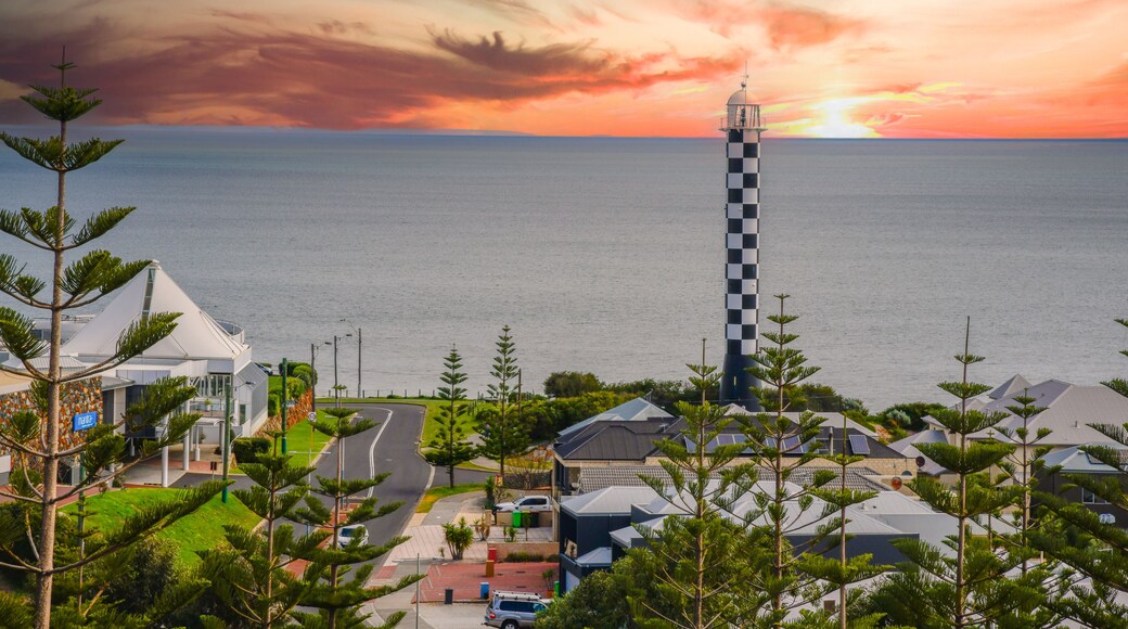 A coastal town with a lighthouse, residential buildings, and a clear view of the sea.