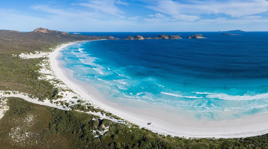 A coastal landscape with a white sandy beach, clear blue waters, and green vegetation.