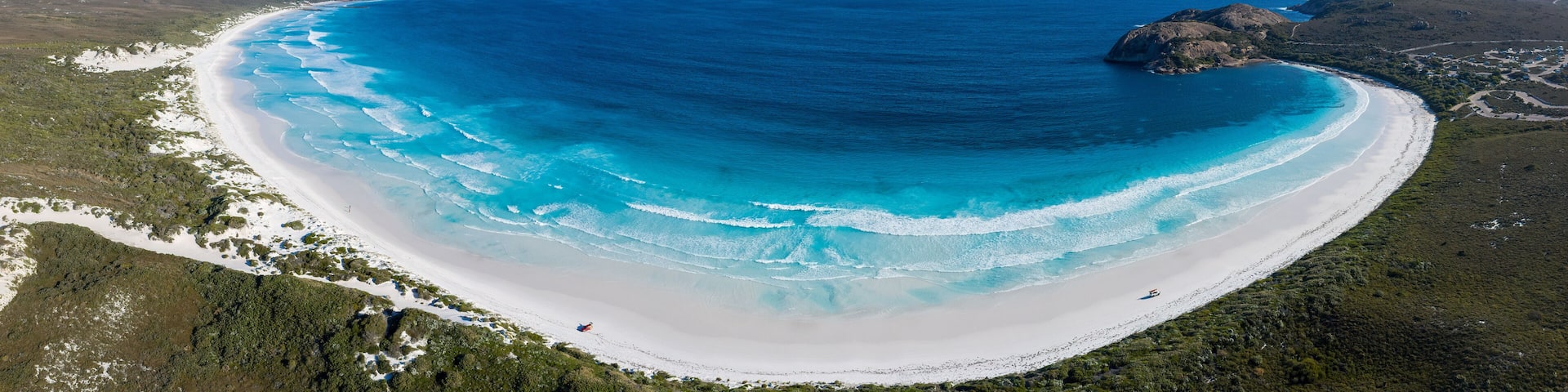 A coastal landscape with a white sandy beach, clear blue waters, and green vegetation.